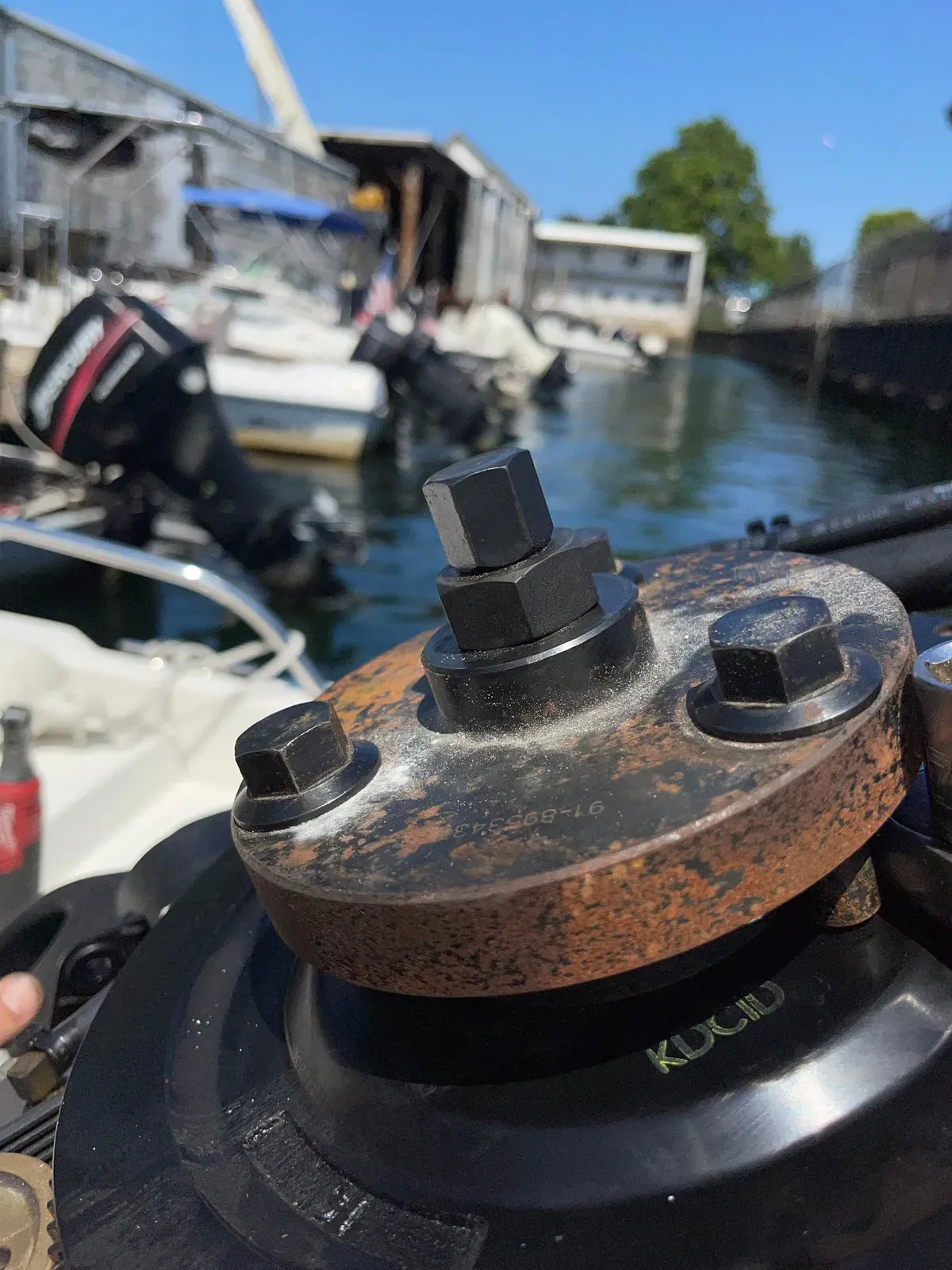 Close-up of a Mercury gearcase mounting flange and its bolts part way through a dockside service, boats in their slips behind.