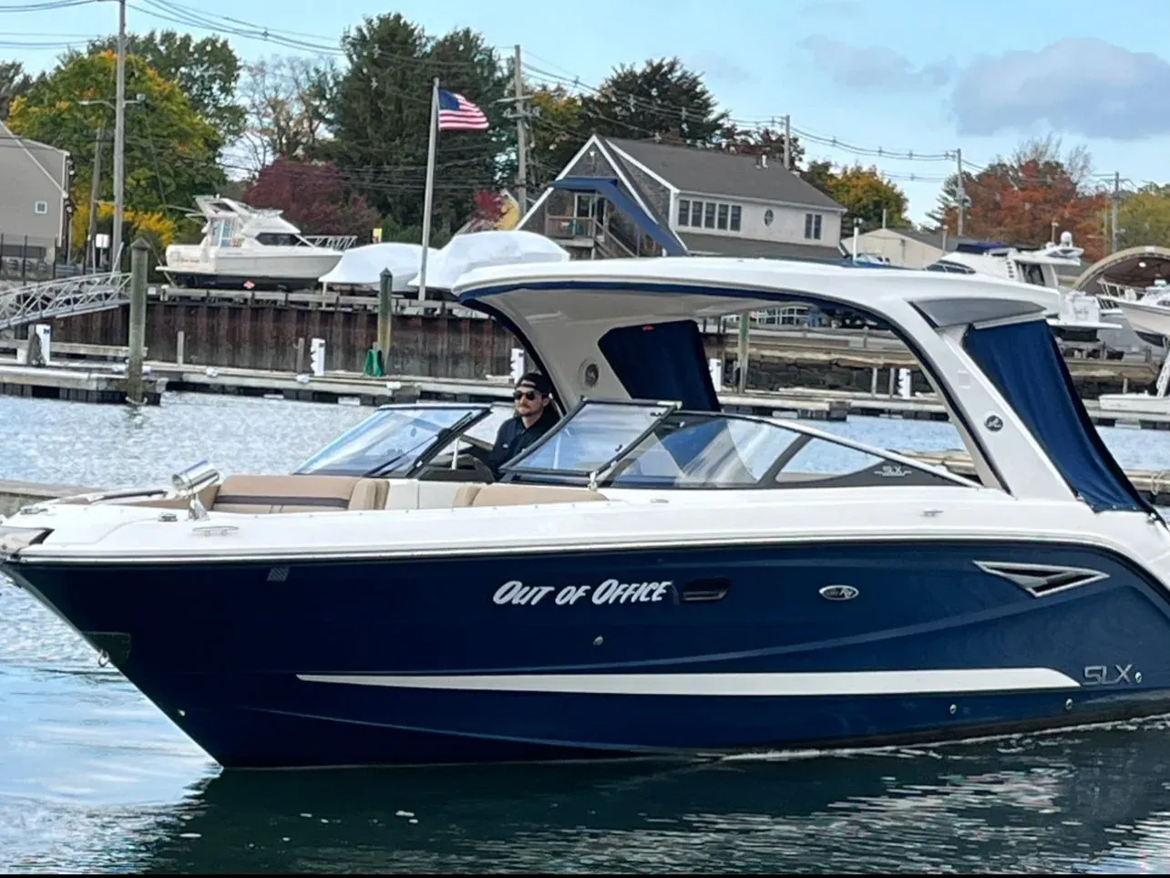 A navy and white Sea Ray SLX tied at a New Hampshire dock in autumn, an owner at the helm and turning foliage on the far shore.