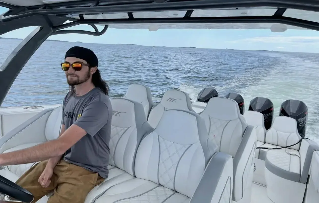 A Mainline Marine technician at the helm of a quad-outboard center console under way on open water, wake spreading behind the Mercury engines.