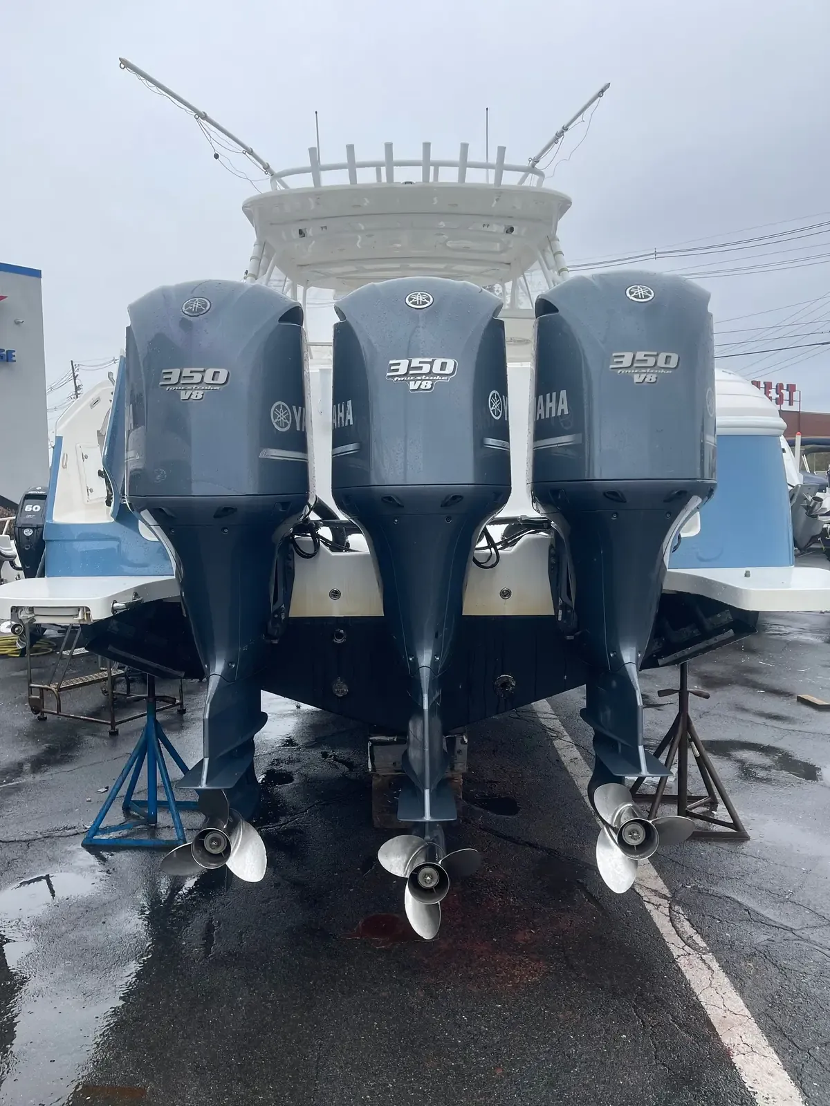 Three Yamaha 350 four-stroke V8 outboards on the transom of a center console standing on jack stands in a boatyard on a wet day.